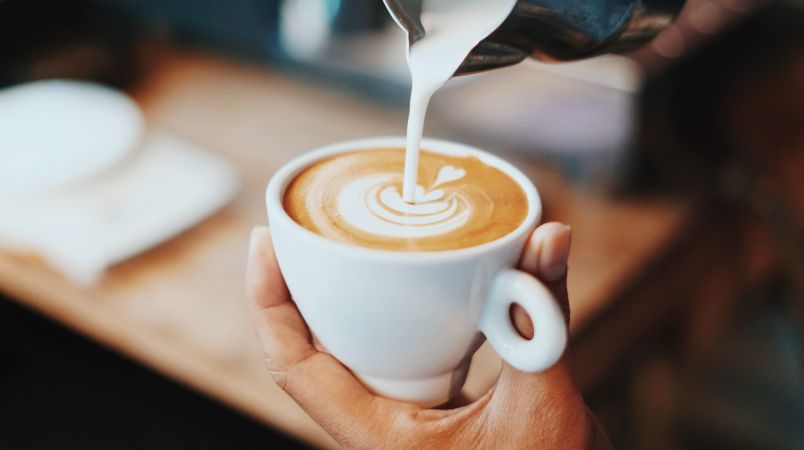 Person pouring latte into a white mug