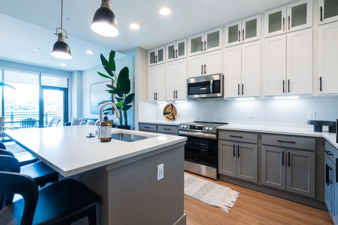 Open concept layout in luxury apartment showing a large floating kitchen island, large sink, floor to ceiling windows, and a large living room space