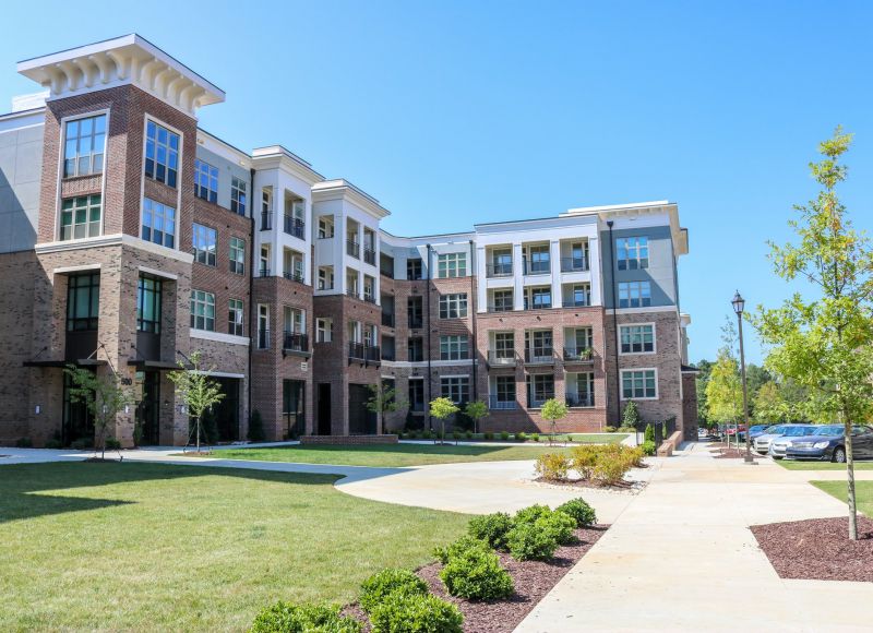 Exterior of Carraway Village apartments showing apartment building, grass area, and native plants around sidewalk