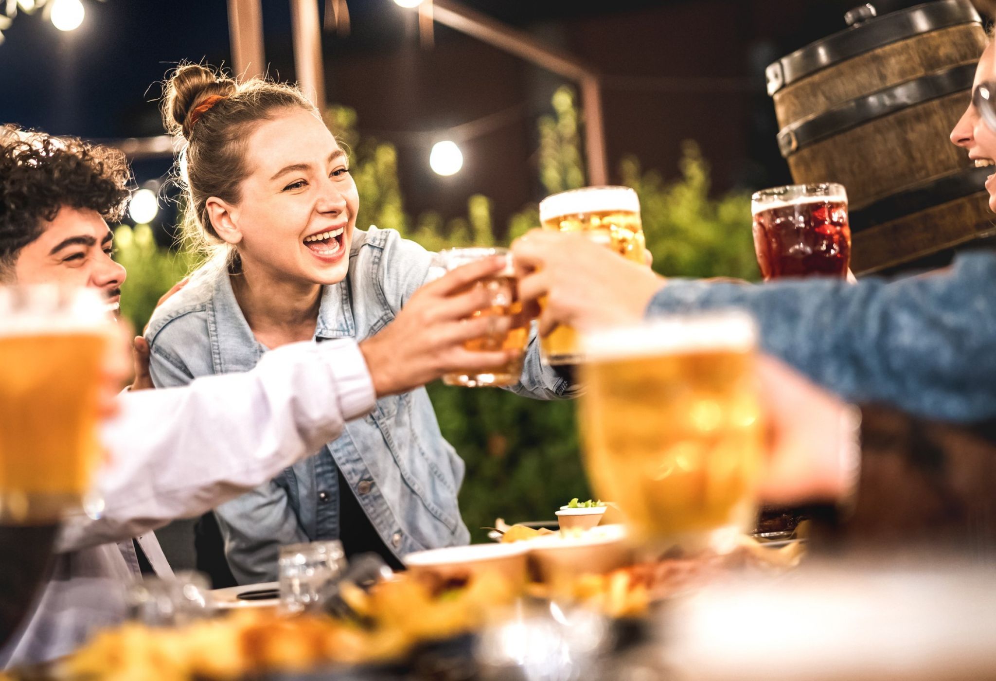 Happy friends clinking and toasting beer at beer garden patio - Life style and beverage concept with young people having fun together out side at patio garden by night